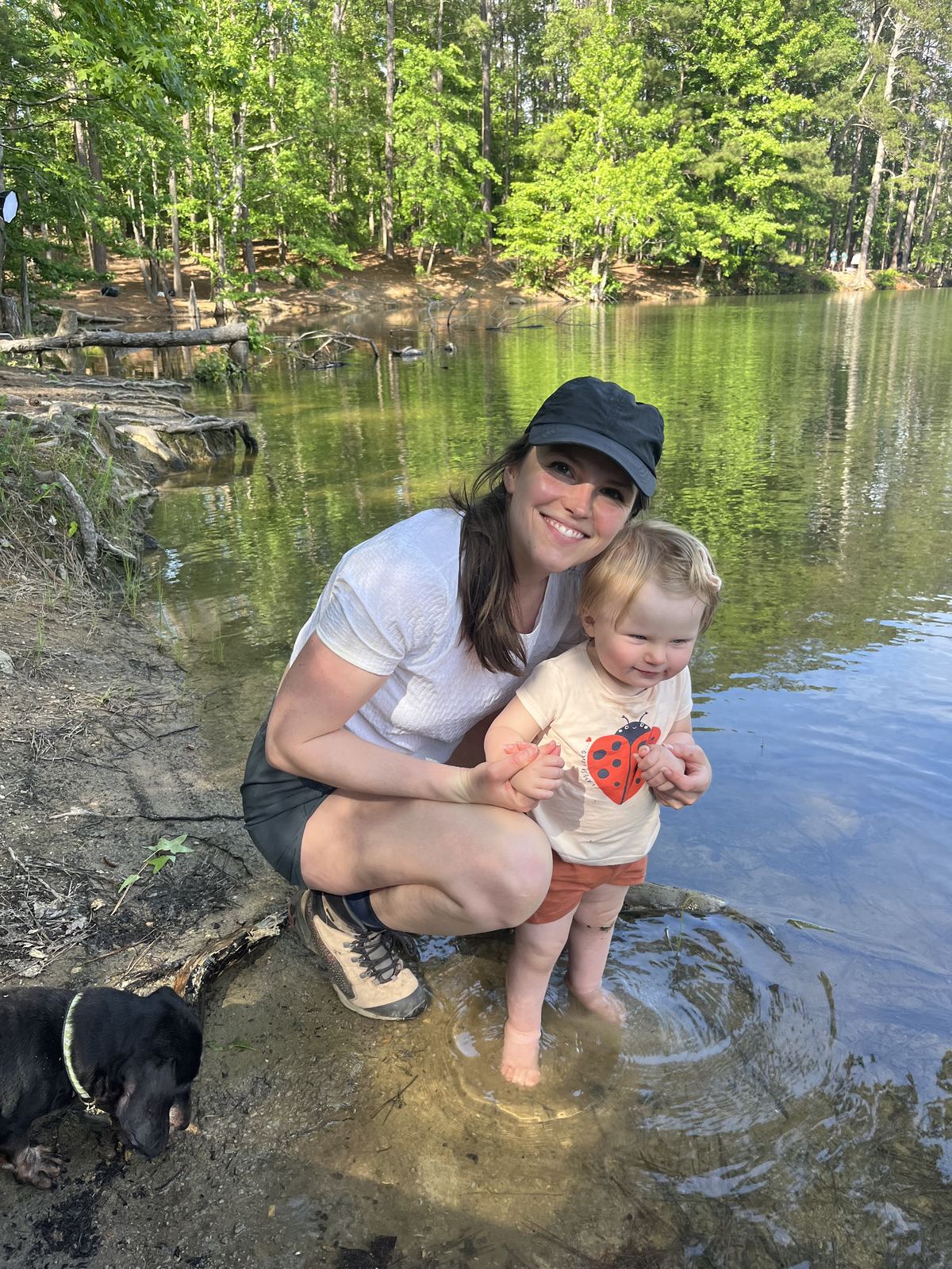 Rachel and her daughter smiling together at a lake, with their dog nearby